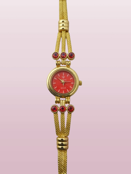 golden bracelet watch with red face and red stones with pink backround